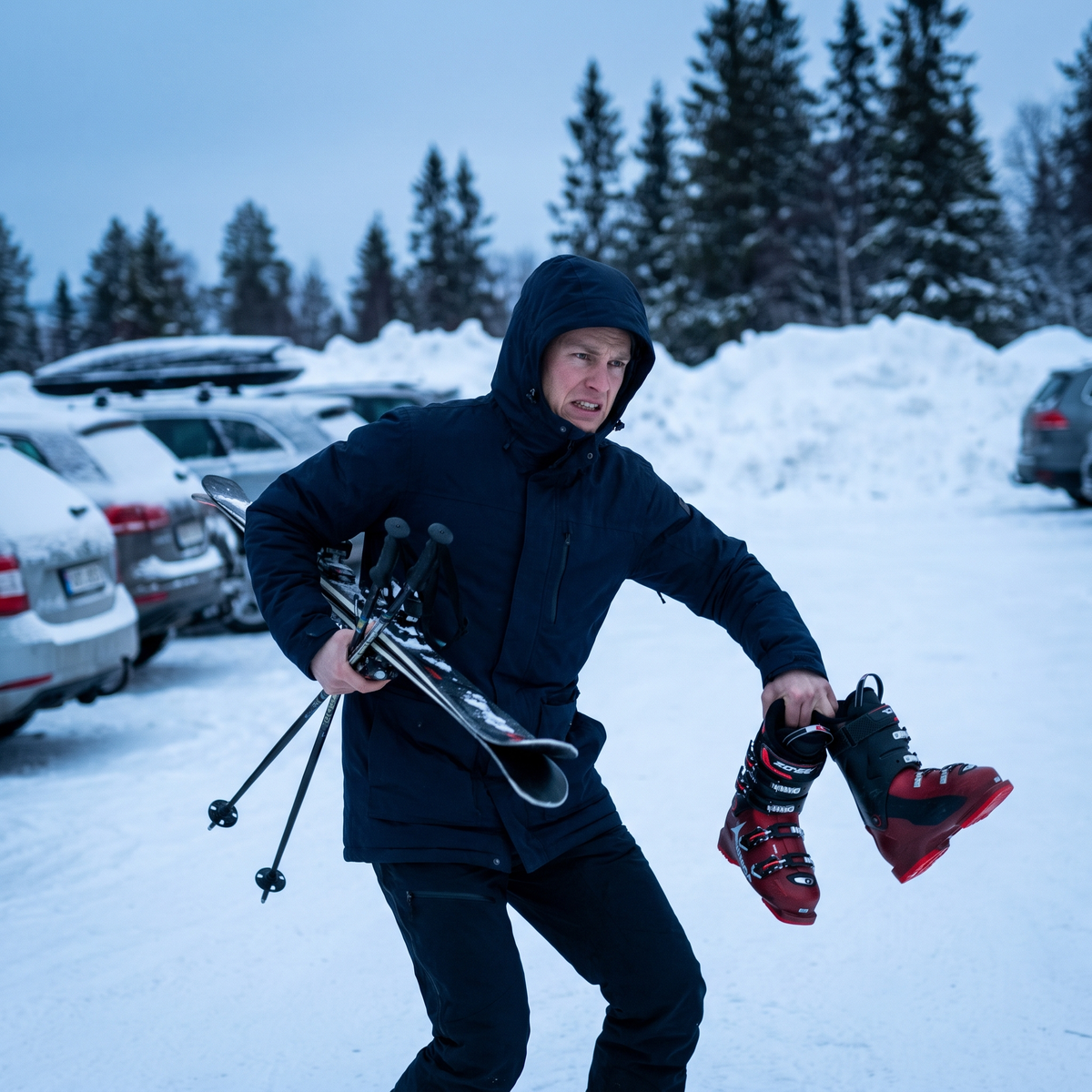 Skidåkare på parkeringen med skidor och stavar under armen och pjäxorna hängande i fingrarna